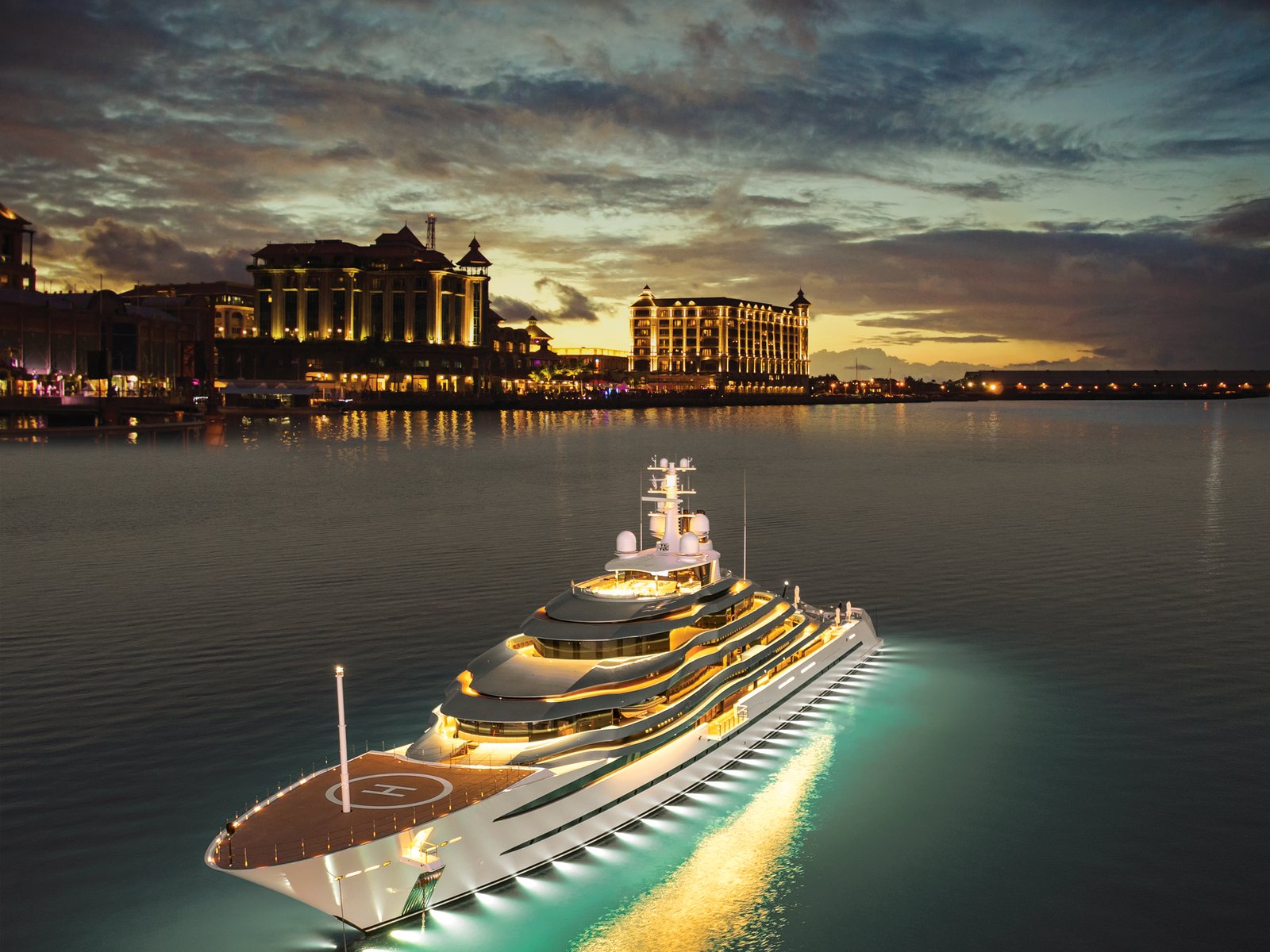 A yacht moored at a marina at dusk, with a lit waterfront beyond